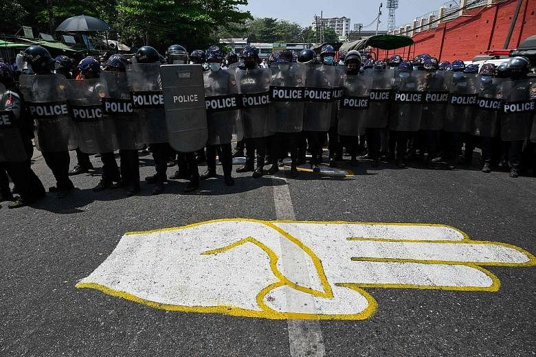 Riot police standing guard in Yangon yesterday behind a drawing on the road of the anti-coup protesters' symbol - a three-finger salute. Four protesters have been killed in crackdowns, whereas the military has reported the death of at least one polic