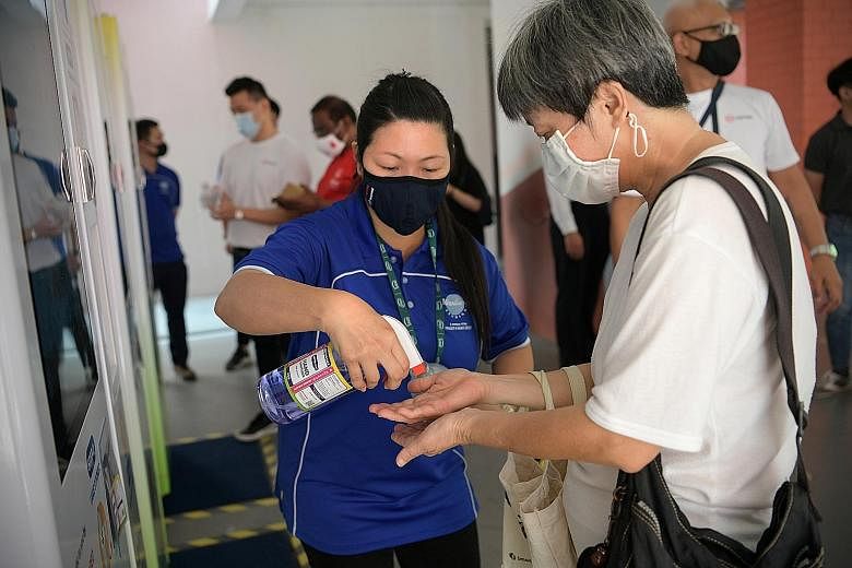 Vending machine assistant Tang Li Ring, 44, letting a resident try out the zero-alcohol sanitiser in Choa Chu Kang yesterday. The Temasek Foundation initiative uses machines that mix sanitiser concentrate with clean water and dispense the ready-to-us
