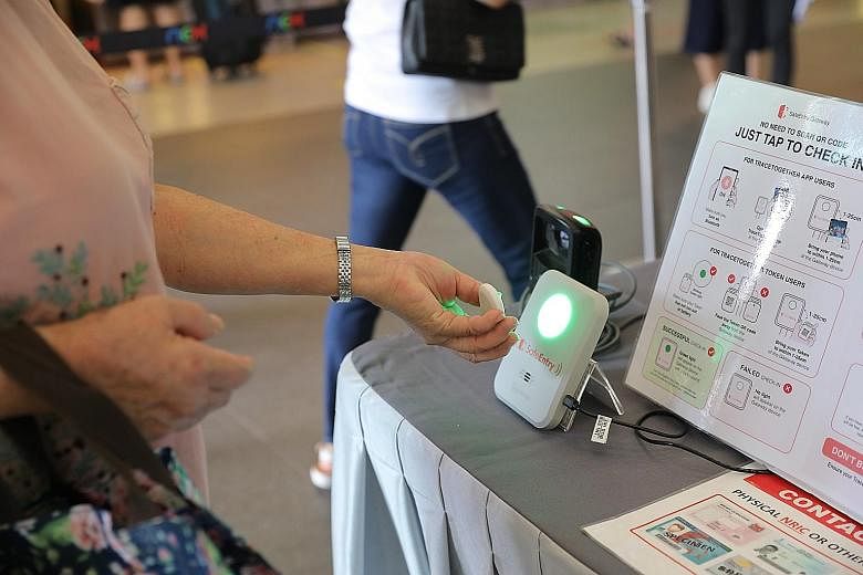 A shopper using the TraceTogether token to check in at Nex mall. Use of TraceTogether will be mandatory in places like malls, workplaces, schools and dine-in food and beverage outlets, but the SafeEntry check-in requirement at individual retail outle