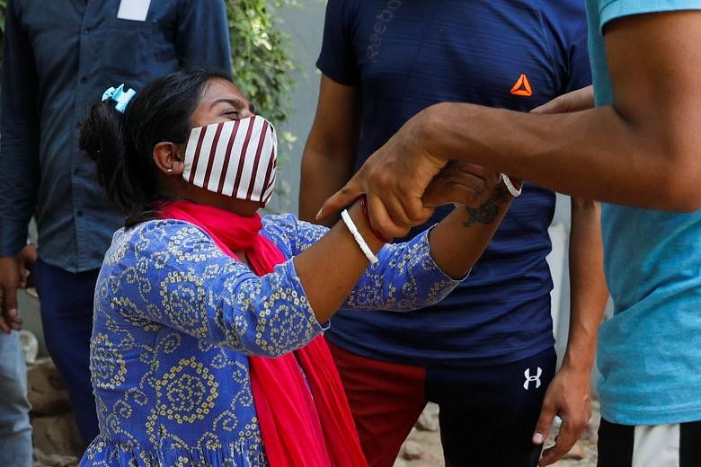 From left: Relatives collecting the remains of Covid-19 victims after a mass cremation in New Delhi on Friday; Ms Shruti Saha, who had been waiting since Tuesday night for her turn to refill an oxygen cylinder for her mother, breaking down after hear