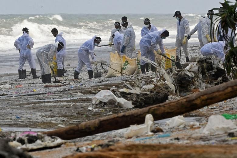 Members of the Sri Lankan Navy (top) removing debris washed ashore from the X-Press Pearl (above) on a beach in Colombo on Monday. The ship, which had nitric acid and other chemicals on board, was on its way to Singapore from India when the fire brok