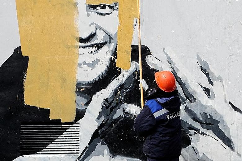 A worker painting over graffiti depicting jailed opposition politician Alexei Navalny in St Petersburg, Russia, in April. The graffiti referred to him as "The hero of the new age". The ban could spell the end of his anti-corruption organisation and n