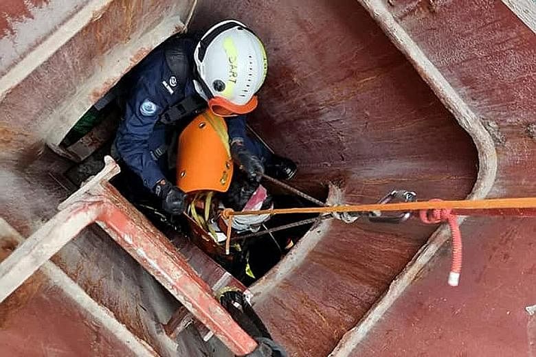 The stretcher carrying the injured worker being manoeuvred through a narrow hatch. The worker fell while unloading steel pipes on board a vessel at Jurong Port on Thursday. Right: SCDF officers treating the worker.
