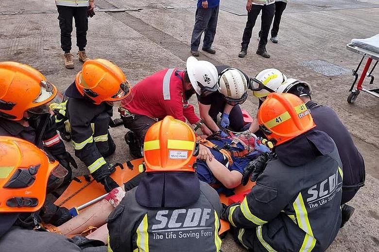 The stretcher carrying the injured worker being manoeuvred through a narrow hatch. The worker fell while unloading steel pipes on board a vessel at Jurong Port on Thursday. Right: SCDF officers treating the worker.
