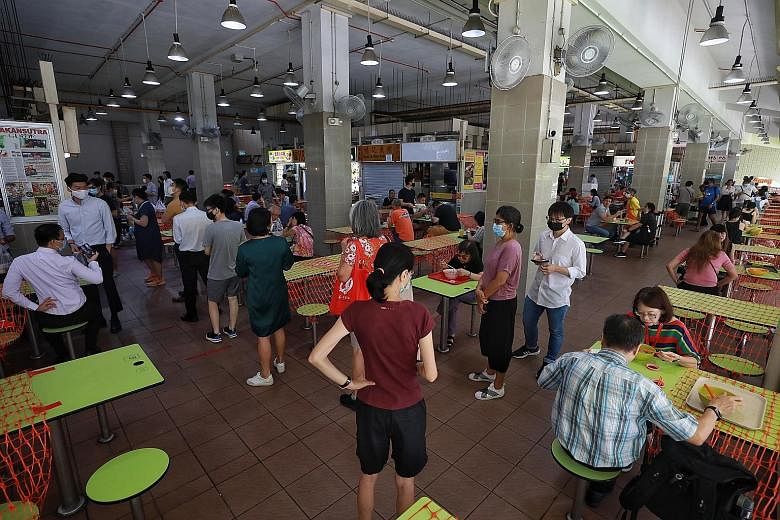 Above: Some stalls at Amoy Street Food Centre saw queues of 10 to 15 people each during lunchtime yesterday, as tables filled up quickly and diners kept to the rule of two. Below: A safe distancing ambassador advising a diner to put on his mask when 