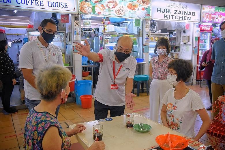 A National Environment Agency officer, with Senior Minister of State Amy Khor (standing, right), reminding patrons at North Bridge Road Market and Food Centre yesterday to clear their used plates.