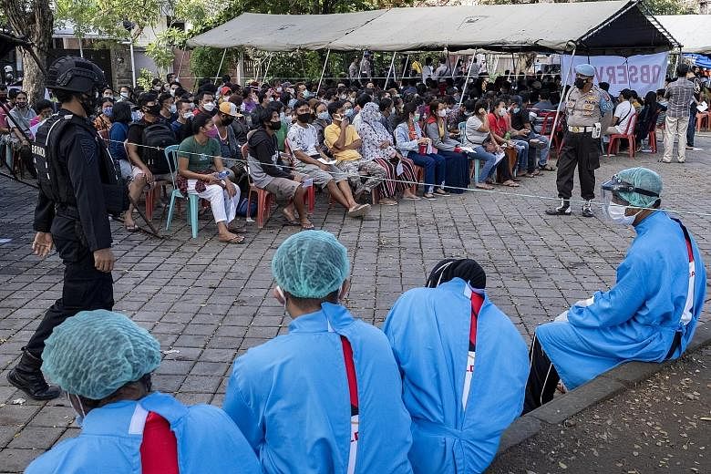 People waiting their turn during a mass vaccination drive in Denpasar, Bali, late last month. Java and Bali have about 1.52 million cases, or 70 per cent of the total number of cases in Indonesia. Workers wearing personal protective equipment lowerin