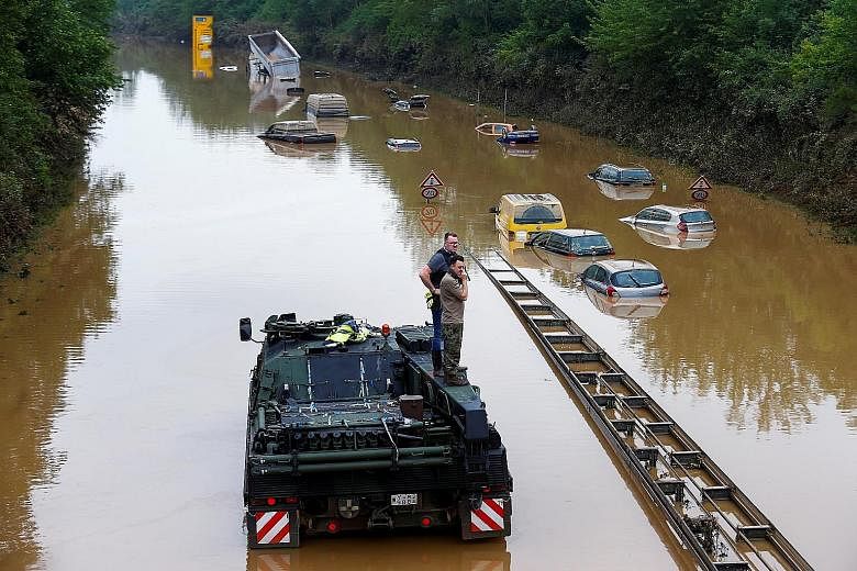 A police officer and a member of the German armed forces standing on a vehicle among partially submerged cars on a flooded road following heavy rain in Erftstadt-Blessem, Germany, yesterday. More than 130 people are dead and 1,300 unaccounted for aft