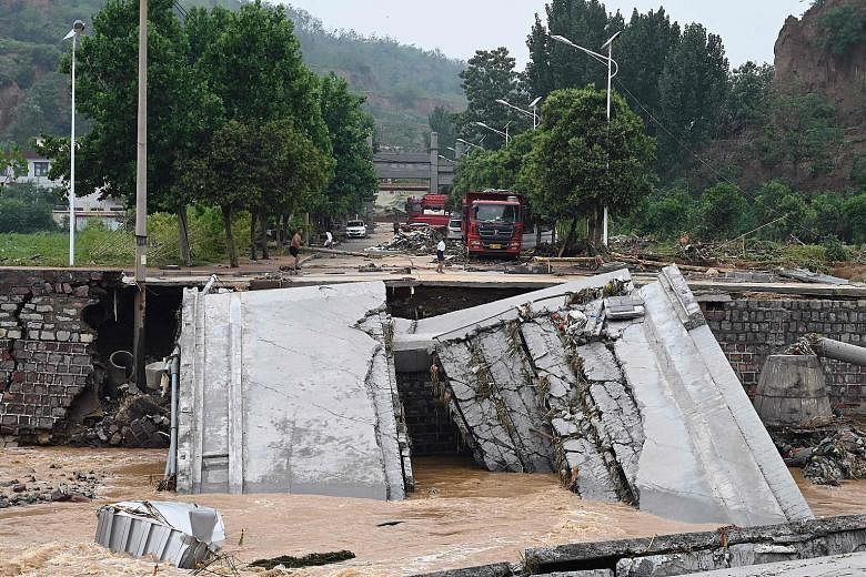 Left: People riding on a front loader as they made their way through a flooded road following heavy rainfall in Zhengzhou, China's Henan province, yesterday. PHOTO: REUTERS Below: A road damaged by severe flooding and a landslide in the county-level 