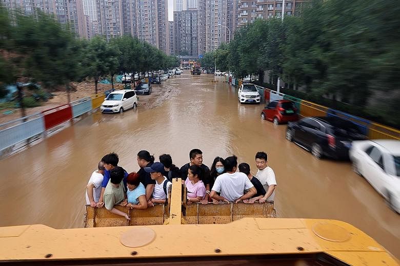 Left: People riding on a front loader as they made their way through a flooded road following heavy rainfall in Zhengzhou, China's Henan province, yesterday. PHOTO: REUTERS Below: A road damaged by severe flooding and a landslide in the county-level 