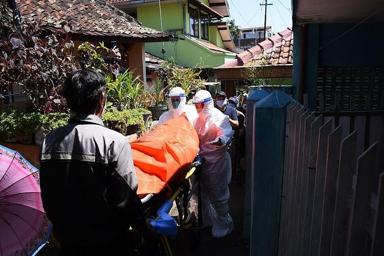 Health workers removing the body of a Covid-19 victim who died at home in Bandung, Indonesia, yesterday. Data from a citizen data platform shows 2,705 have died at home from Covid-19 in the last two months.