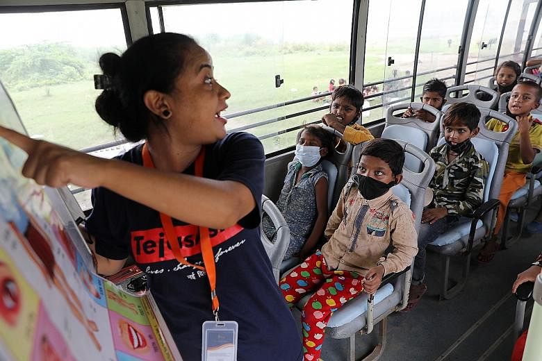 A woman teaching children (above) in a bus run by non-governmental organisation (NGO) TejasAsia on Monday and children holding up their slate chalkboards (right) in their mobile classroom. The NGO uses "Hope Buses", as the classrooms are called, for 