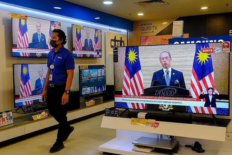 Malaysian Prime Minister Muhyiddin Yassin is seen on television monitors at a store in Kuala Lumpur on Monday, at a press conference announcing his resignation. Having a bipartisan government would enable the incoming prime minister to survive confid