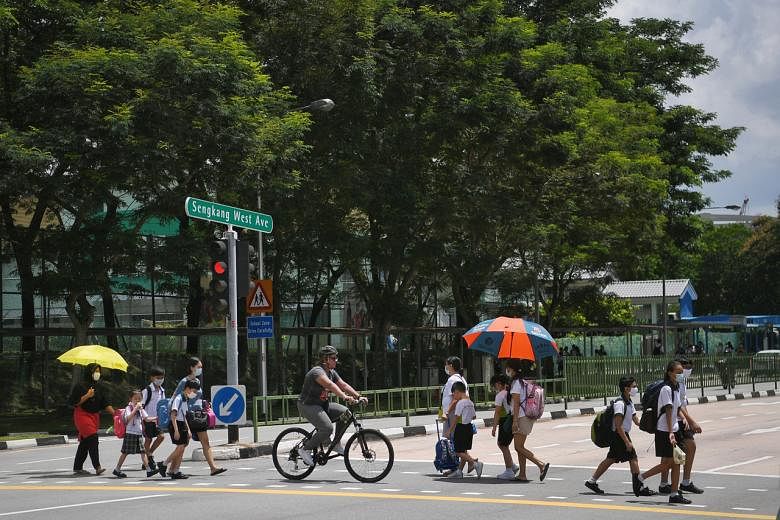 <p>Primary school children and their parents cross a traffic junction at Sengkang West Ave with umbrellas to shield themselves from the afternoon sun, taken on Aug 21, 2020.</p>
