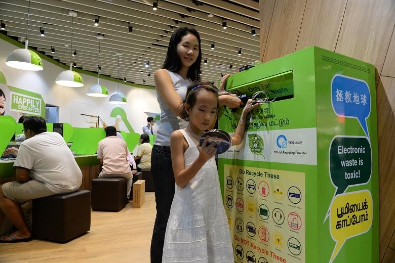 Ms Bernadette Ng and her daughter, Clare Tan Min, eight, dropping several old electronic items in the recycling box at the StarHub outlet in Tampines Mall. Ms Ng says she makes it a point to have her children present when she donates recyclables.