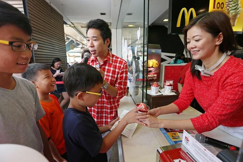 Local celebrities Chua En Lai and Michelle Chong selling strawberry sundaes to (from left) Ethan Loh-Chan, 12, Ernest Tan, nine, and Ethan Tan, 12, at a McDonald's in Ang Mo Kio yesterday. From Nov 1 to 15, McDonald's will donate $1 from every strawb