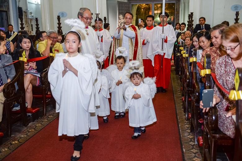 Father Ignatius Yeo, led by little "angels", carrying a statue of the baby Jesus into St Joseph's Church. Looking on as the children trooped past is conductor and director of the Cathedral Choir of the Risen Christ, Dr Peter Low, who composed a carol