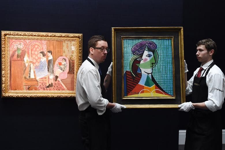 Staff carry the painting Tete De Femme by Pablo Piccaso next to Henri Matisse's work La Lecon De Piano during a press preview at Sotheby's auction house ahead of its auction tomorrow.
