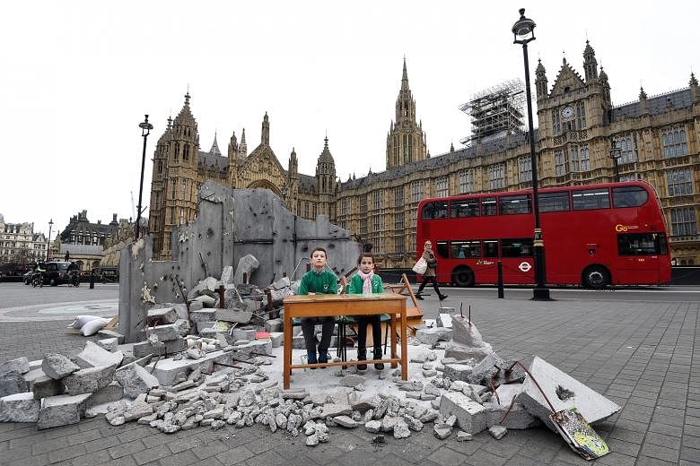Abdallah, 12, and Dania, 10 - whose school in Aleppo, Syria, was bombed - sitting amid a mock-up of a destroyed classroom outside the Houses of Parliament in London yesterday. The photo-call was organised by Save The Children to highlight the need fo