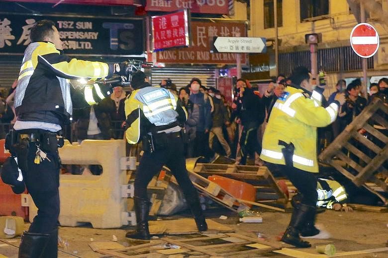 A policeman pointing his pistol (left) during the riot at Mongkok district in Hong Kong. Demonstrators charged police lines with home-made shields and set rubbish on fire in the worst street violence the city has seen since pro-democracy protests in 