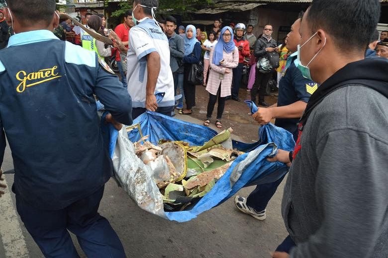 Officials taking away wreckage from a military plane that crashed into a house in a densely populated area in Malang, East Java, yesterday while on a test flight from the local air force base.