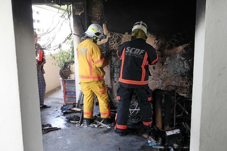 SCDF officers examining the scene of a fire that started outside an HDB flat on the seventh floor of Block 18, Eunos Crescent, yesterday. The blaze was put out by residents armed with buckets of water.