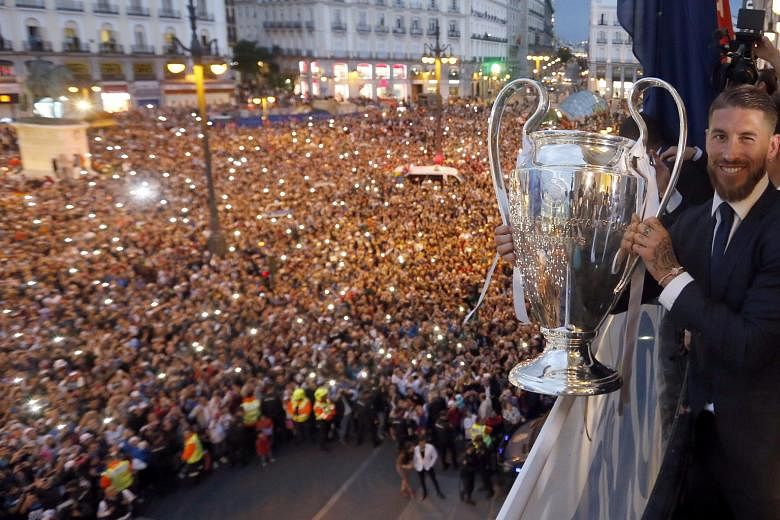 Real skipper Sergio Ramos holding the Champions League trophy on the balcony of the Madrid Autonomous Government's headquarters, as thousands of frenzied fans cheer during the celebrations.