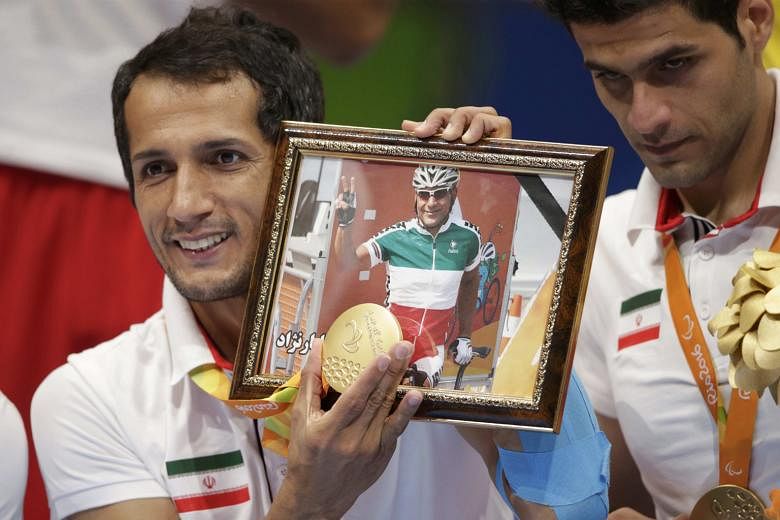 Ramezan Salehihajikolaei of the Iran sitting volleyball team holding his gold medal and a photograph of Iranian cyclist Bahman Golbarnezhad.