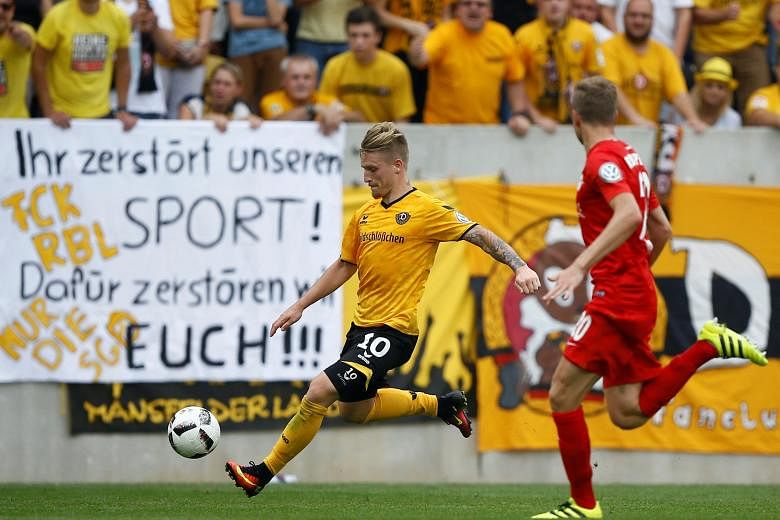Dynamo Dresden's Marvin Stefaniak (in yellow) in German Cup action with RB Leipzig's Benno Schmitz. The banner that was displayed by Dynamo fans reads: "You destroy our sport! For this we will destroy you!!!"