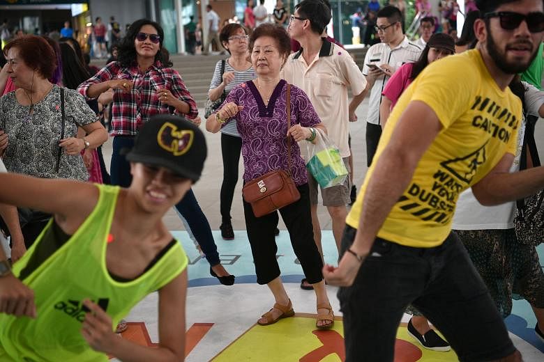 Madam Tan (centre, who declined to give her full name but said she is in her 70s) dancing with a plastic bag containing cakes at Bedok Town Square on Sunday. She was among almost 1,000 members of the public who took part in Unlock And Roll, an event 