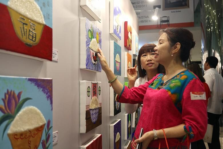 Ms Belinda Chua (in white), 53, wife of artist Tan Kay Nguan, showing a guest a painting for sale at Marina Square Linkbridge Atrium yesterday. More than a hundred rice bowls, painted on canvas with acrylic, adorned the space, as part of a charity dr