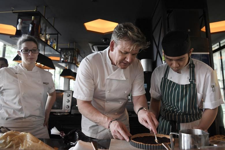 British restaurateur Gordon Ramsay shows Bread Street Kitchen intern Ong Sao Wee how to spread blueberry paste for the blueberry- almond tart creme fraiche. Standing behind them is the restaurant's executive chef Sabrina Stillhart.