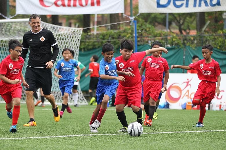 Children aged six to 12 years old playing football at Jurong East Stadium as ActiveSG Football Academy principal Aleksandar Duric, a former Lion, looks on. The academy will merge its junior programme with the FAS' Cubs Programme.