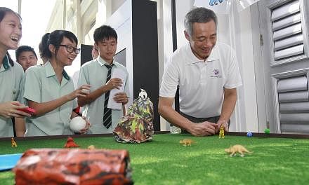 Prime Minister Lee Hsien Loong flicks a marble past obstacles and towards a hole on a Jurassic Park-themed game during Singapore Heritage Fest's 10th anniversary celebrations at the the National Museum of Singapore&nbsp;on Sunday, July 21, 2013. A ne