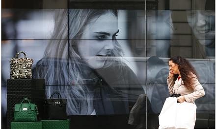 &nbsp;A woman walks past a video display in the shop window of a Mulberry store in central London on Oct 14, 2014.&nbsp;The ailing British luxury goods brand Mulberry has appointed Johnny Coca as its new creative director. -- PHOTO: REUTERS