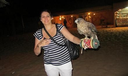 Ms Katherine Cole extending a hand to a bird of prey at a falcon show in the Arabian Desert.