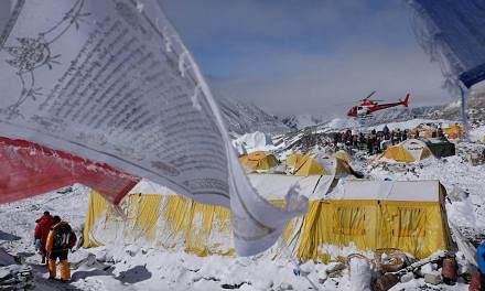 This April 26, 2015, photo shows Buddhist prayer flags fluttering in the wind near tents as a rescue helicopter takes off from Everest Base Camp, after an earthquake-triggered avalanche crashed through parts of the base camp, killing scores of people