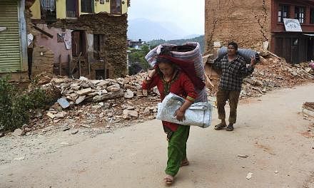 Nepalese residents carry their belongings as they walk past destroyed buildings in&nbsp;the town of Chautara in north-eastern Nepal in the aftermath of two earthquakes in the span of three weeks that shook the country. -- PHOTO: AFP