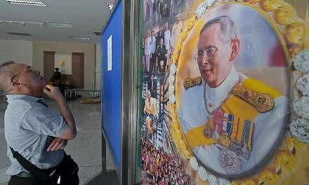 A Thai well-wisher reads a statment from the royal bureau next to a portrait of Thai King Bhumibol at Siriraj hospital in Bangkok on June 1, 2015. Thailand's junta has banned a journalists' association from holding a debate on controversial lese maje