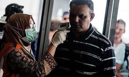 An airport health official checking the temperature of passengers from Singapore at Yogyakarta Airport yesterday.