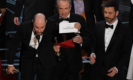 La La Land producer Jordan Horowitz holding up the card showing Moonlight as Best Picture winner, as presenter Warren Beatty (centre) and host Jimmy Kimmel look on.