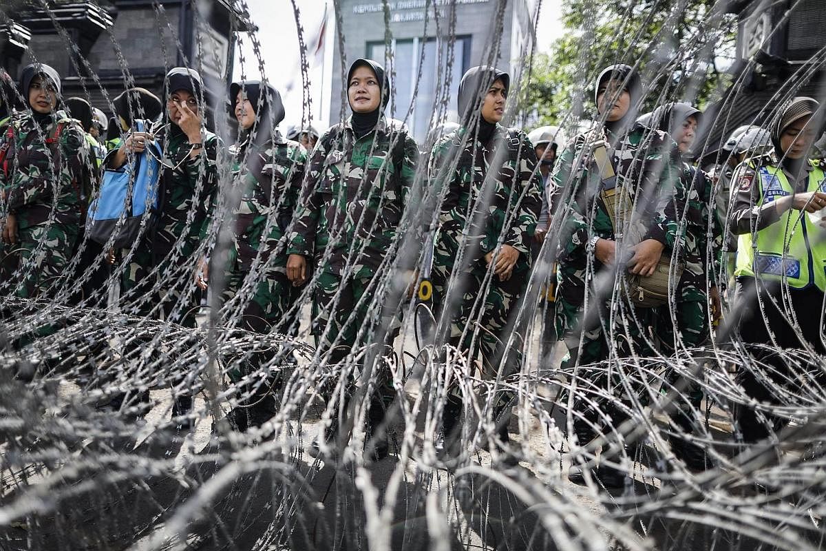 Military personnel (far left) on guard outside the Jakarta police HQ last month as cleric Rizieq Shibab (left) arrived for questioning over allegations of defamation. Jakarta Governor Basuki Tjahaja Purnama at a concert last week ahead of this month'