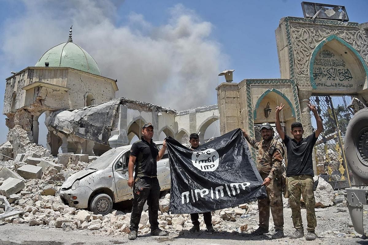 Members of the Iraqi Counter-Terrorism Service proudly displaying an upside-down black flag of ISIS outside the destroyed Al-Nuri Mosque in the Old City of Mosul after the area was retaken late last month.