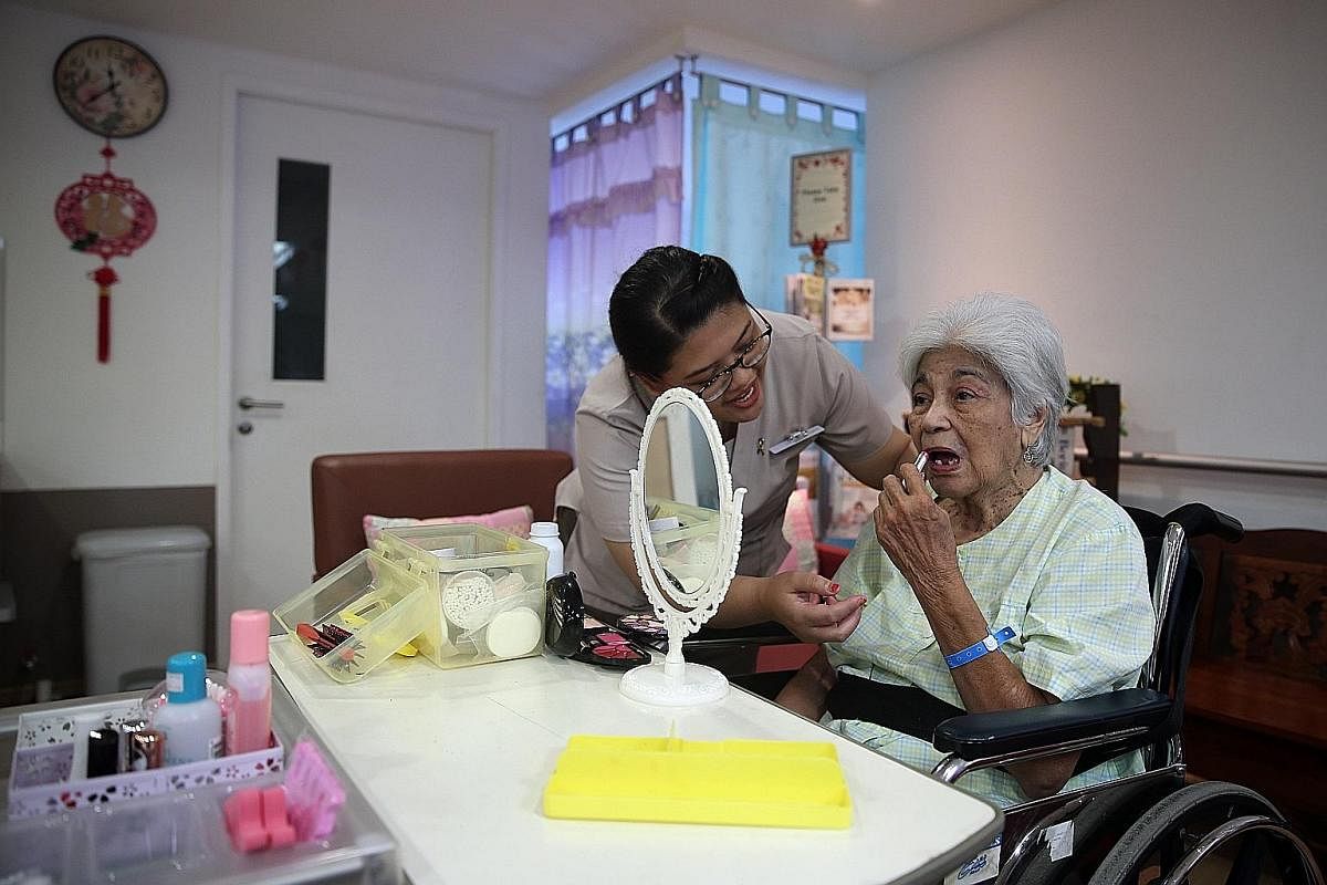 Senior nurse manager Lee Soh Luan wheels Madam Wong Soo Han, 87, near Madam Goh Chor Keng, 88, as they show off their dolls. Both patients have dementia and Madam Wong was admitted to hospital because of a fracture after a fall while Madam Goh had vi