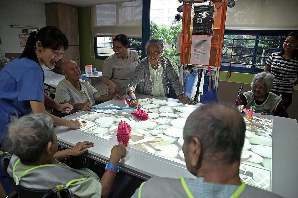 Senior nurse manager Lee Soh Luan wheels Madam Wong Soo Han, 87, near Madam Goh Chor Keng, 88, as they show off their dolls. Both patients have dementia and Madam Wong was admitted to hospital because of a fracture after a fall while Madam Goh had vi