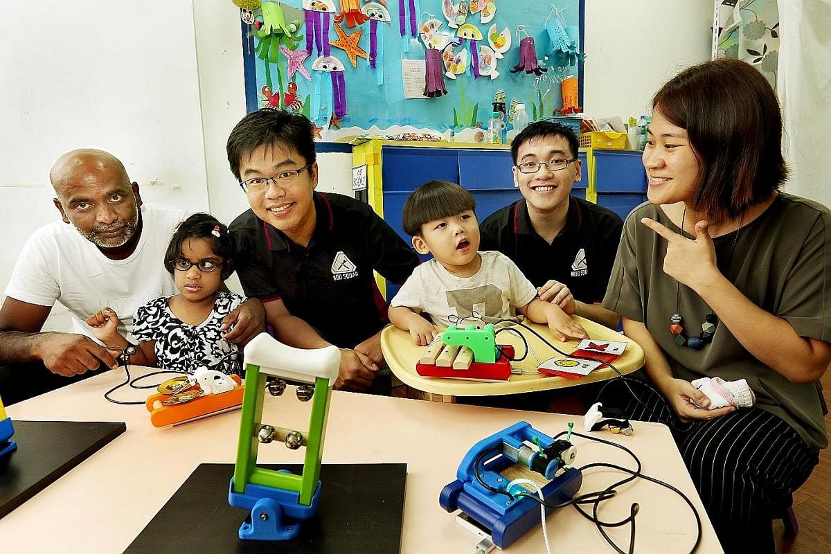 Mr Jain Rathan with his daughter Mackenzia Gabriella and Mrs Teo Wei Lin with her son Reon. The children are playing with the modified musical instruments created by engineers from DSO National Laboratories, Mr Yee Qing Xiang (third from left) and Mr