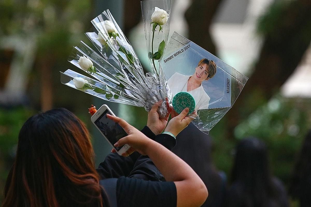 A fan takes photos of a picture of SHINee's lead singer Kim Jong Hyun, who died on Monday, at a memorial service held for him at Hong Lim Park. From left: South Korean rapper G-Dragon; Singaporean singer Ferlyn Wong, a member of the now-defunct K-pop