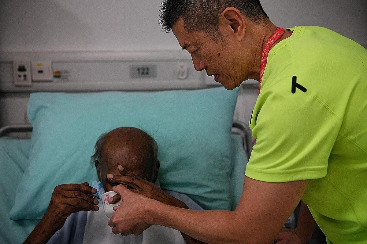 Customer service officer Gary Tee, 50, a volunteer with 20 years of service, helps feed a patient during a befriending session. Befrienders provide companionship and a listening ear to patients, and also to caregivers and family members. They also help pa
