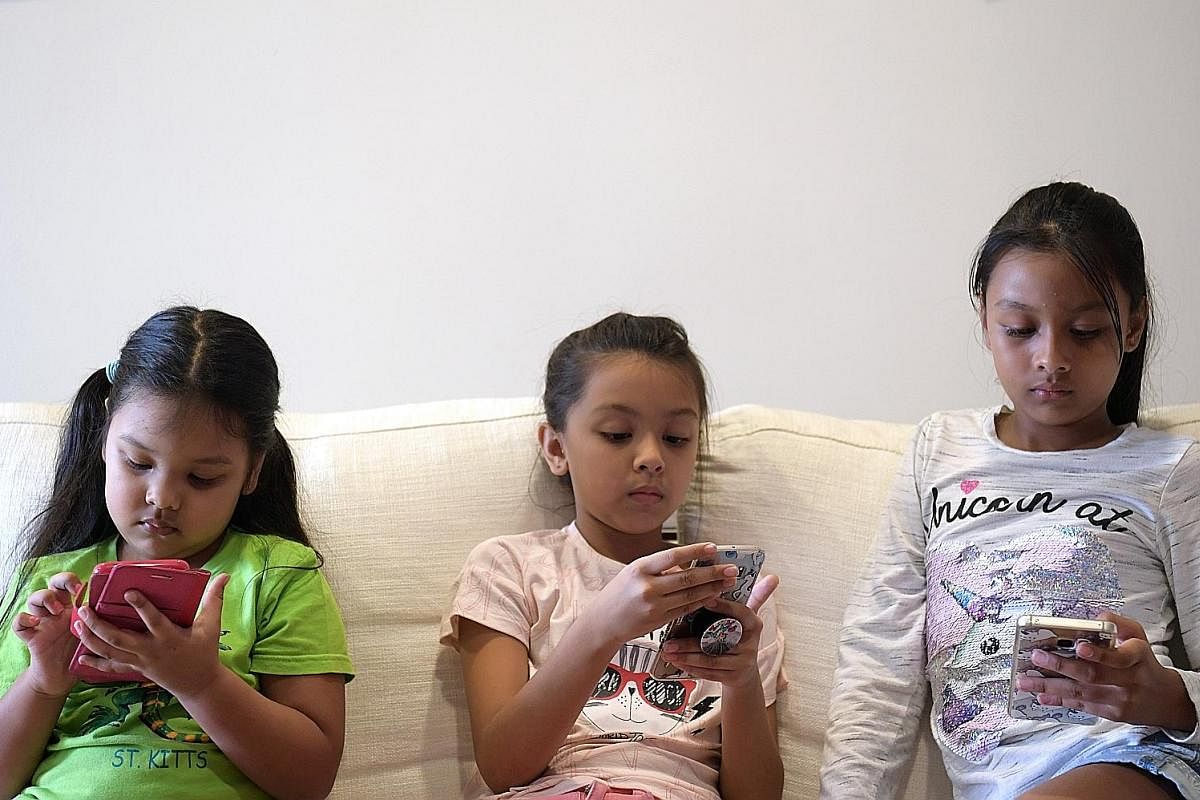 (From far left) Trina Shah, four, and her twin sisters, Tiara and Tania Shah, eight, all have mobile phones. Sisters Gayle Jiow (left), nine, and Genevieve Jiow, 12, with a mobile phone that they share. Ms Kavitha Velayutham gave her daughter Tejaswi
