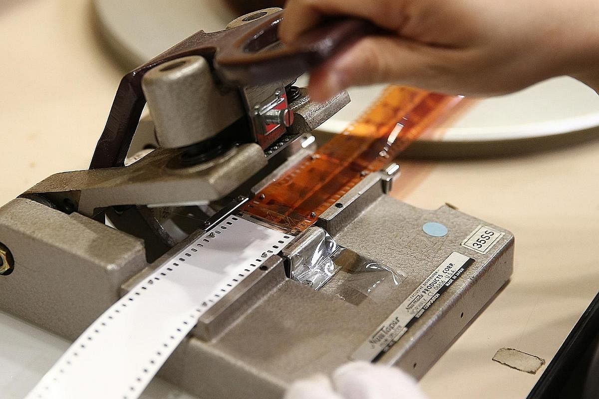 A damaged leader - the length of film attached to the head or tail of a film to assist in threading a projector - is replaced with a new leader using a film splicer. A reel of brittle 16mm film that has shrunk and warped. A film in this state can no 